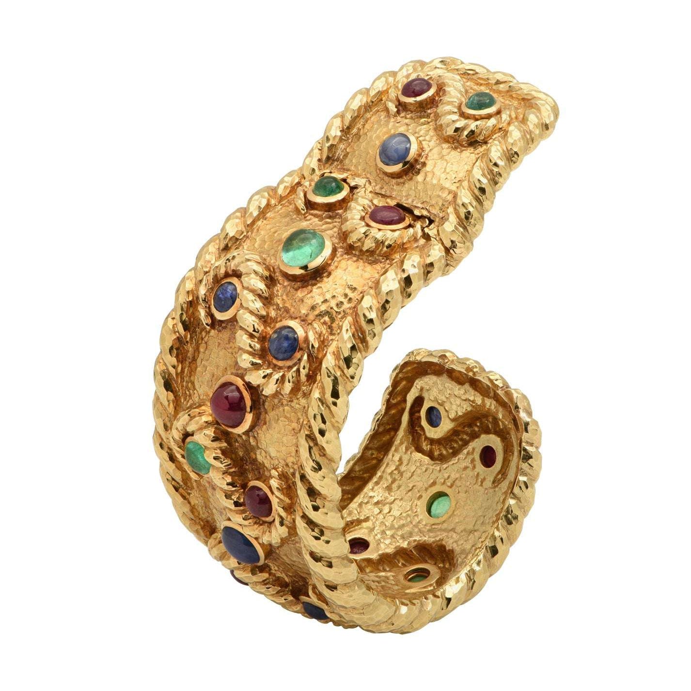 Luxury David Webb 18K Yellow Gold Cuff Bangle Bracelet adorned with 6 Emeralds, 8 Rubies, and 6 Sapphires, highlighting artisanal craftsmanship and a stunning design by Vivid Diamonds.