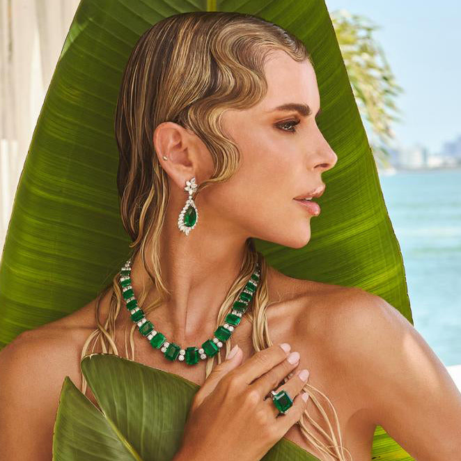 Stunning model adorned with a 103.32 Carat Emerald and Diamond Necklace in Platinum by Vivid Diamonds, showcasing the luxurious design against a tropical backdrop.