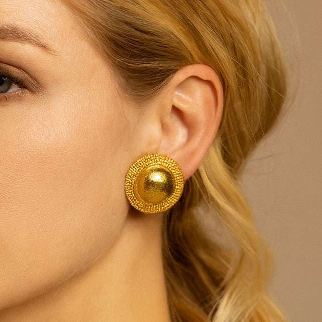 A model wearing Lalounis 18 Karat Yellow Gold Circle Dome Stud Earrings - V50619 by Vivid Diamonds, highlighting the earrings' exquisite craftsmanship and bold elegance against a chic hairstyle.