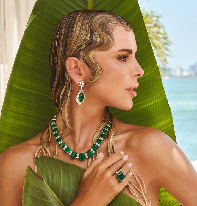 Stunning model adorned with a 103.32 Carat Emerald and Diamond Necklace in Platinum by Vivid Diamonds, showcasing the luxurious design against a tropical backdrop.