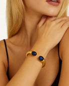 Elegant model showcasing the 18k Yellow Gold Lalounis Sodalite Cuff Bangle by Vivid Diamonds on her wrist, highlighting its luxurious design and vibrant blue stones.